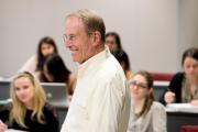 An older faculty member smiles in a classroom of students