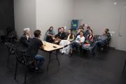 A group of students facing a table in a classroom, with two instructors seated at the front of the table
