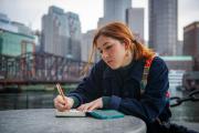 Student writing in a notebook outdoors in Boston