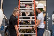 Students maneuvering a ladder within a room; one is wearing a hard hat for protection