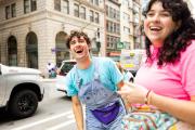 A student wearing overalls and a fanny pack, smiling brightly on Boylston Street