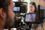 A student looking into a video camera, with another student in the background