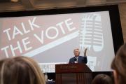 Person at a podium with a projection reading Talk the Vote from behind