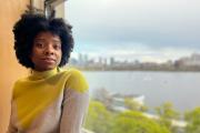 Woman in yellow and white sweater leans on window overlooking Boston