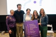 Five panel participants stand smiling at the camera and holding the signage for the panel event.