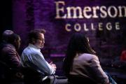 A view of the backs of three panelists sitting on a stage with the Emerson wordmark projected on the wall beside them.