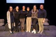 Six panelists stand on a stage smiling at the camera