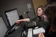 A student pointing toward a monitor, addressing another student sitting next to them