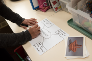 A student drawing a web diagram in permanent marker on a piece of paper. The word "Target" is at the center with questions springing out to the sides, such as "Where do you see it?", "What can you use it for?" and "What are some features?"