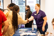 an Emerson employee in a branded shirt shakes the hand of a student over a table