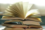 A pile of opened hardcover books, stacked, with one book at the top spread open with flared pages