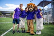 A group of three students posing for a photo with Griff, Emerson College's sports mascot, a lion with a bright orange mane