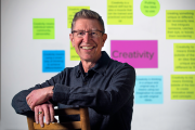 Thomas Vogel wearing a dark blue jacket standing in front of a board highlighting creativity