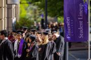 Students in the sidewalk queuing for their ceremony next to a flag that says Student Lineup