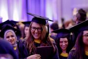 Master’s graduates in their academic hoods at the ceremony, one is laughing.