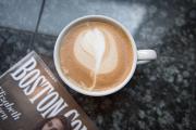 Overhead shot of a cappuccino with a leaf design on a black table next to a magazine