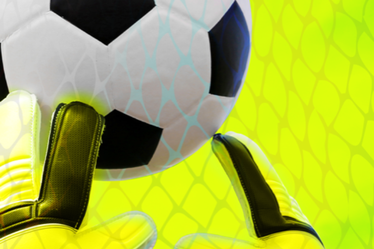 A closeup of a soccer ball approaching a goalie's gloves against a yellow background
