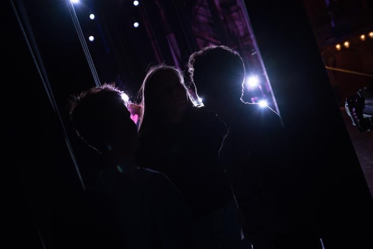 Students standing in the wings of a theatre, looking at the stage