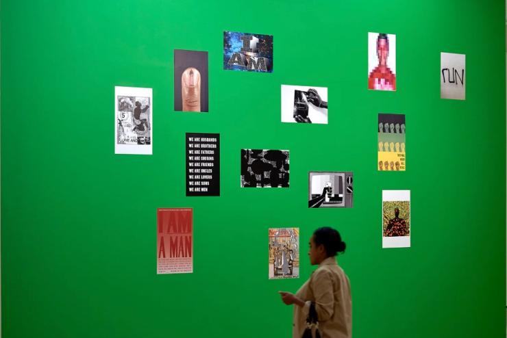 Gallery mock up shows many small posters on a green wall with a person looking at them