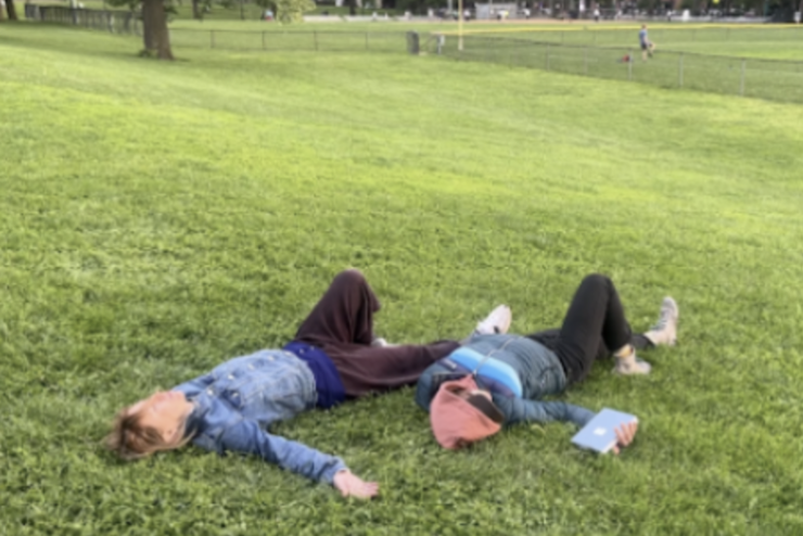 two people lying on the grass in similar positions, one holding a book