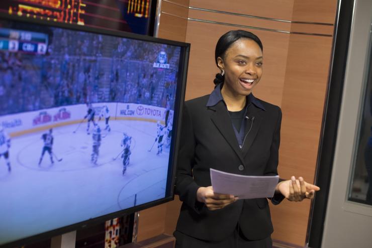 Anchor standing next to tv and holding a file
