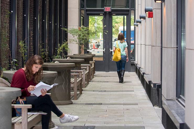 A student sits and reads on campus along a narrow path