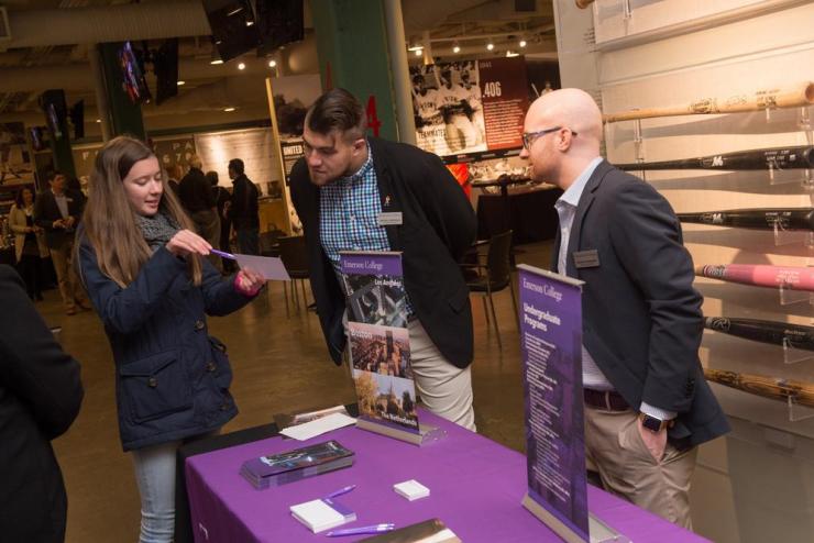 Two people standing at a display table with Emerson College-branded signage