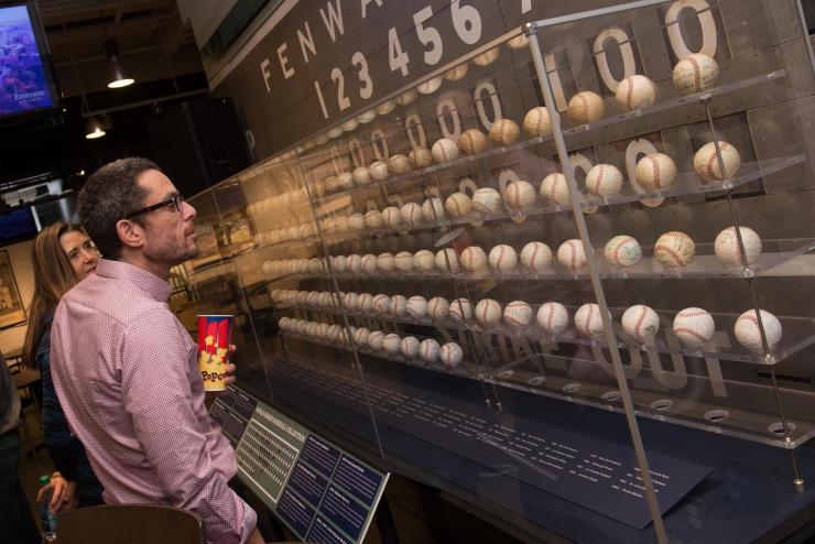 A person looking at rows of old autographed baseballs within a long display case