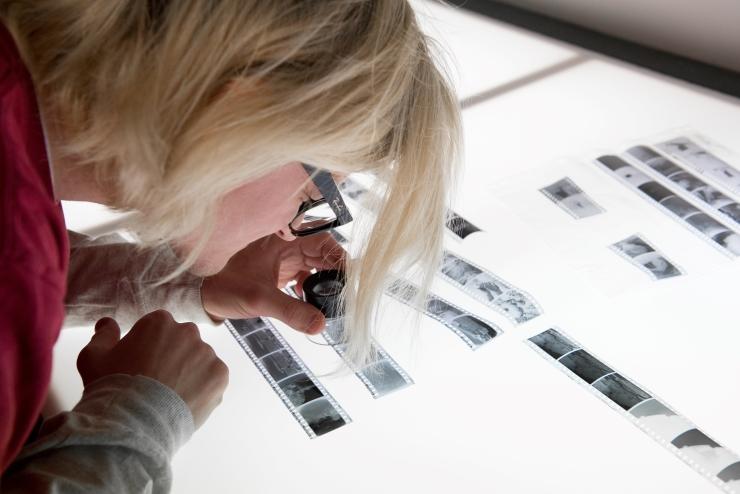 Student looking at photos under magnifying glass in Darkroom