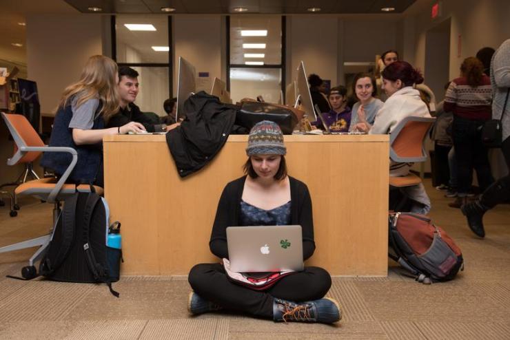 Student sitting on the floor while using their laptop in the Iwasaki Library