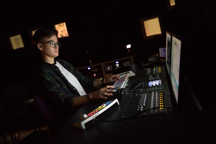Student, illuminated by computer screen, working on audio project