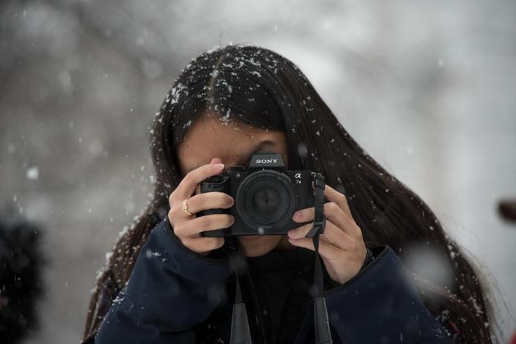 Woman outdoors during a snowy day, peering through a handheld camera