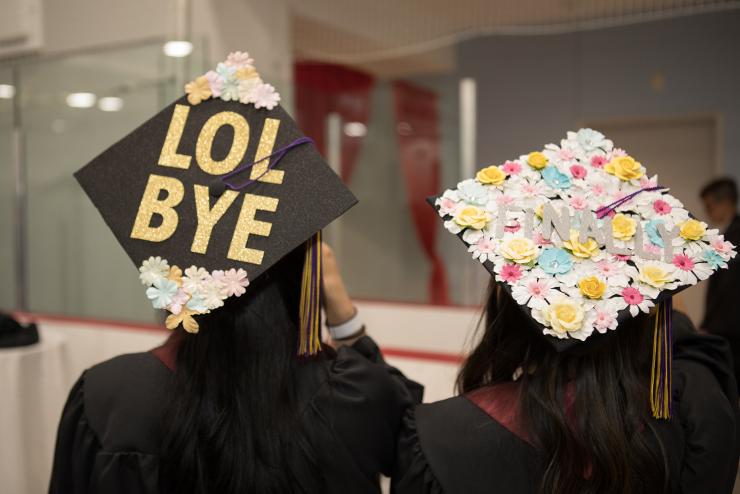 Photo of two students posing with their decorated caps, one states "LOL BYE" while the other states "FINALLY"