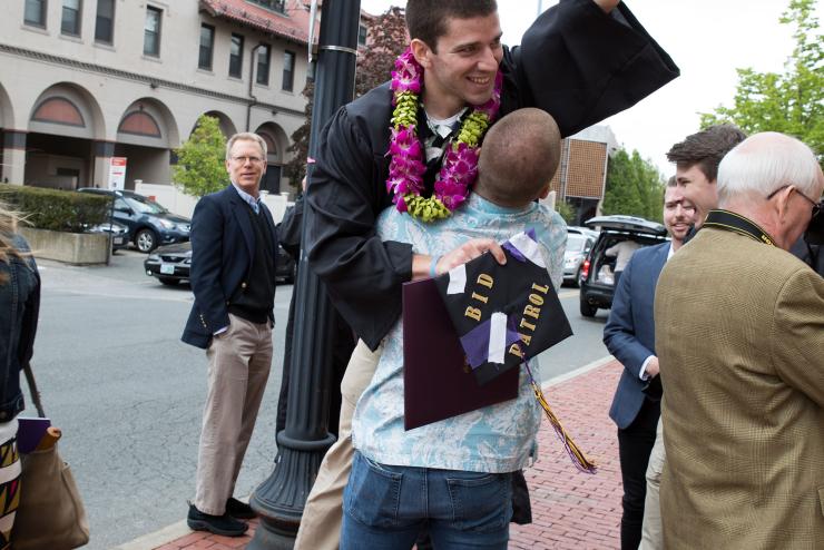 Person picking up graduate who is holding their graduation cap