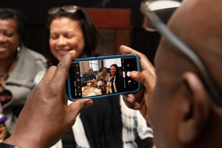 Alumnus at an event taking a photo of three other alums with their phone