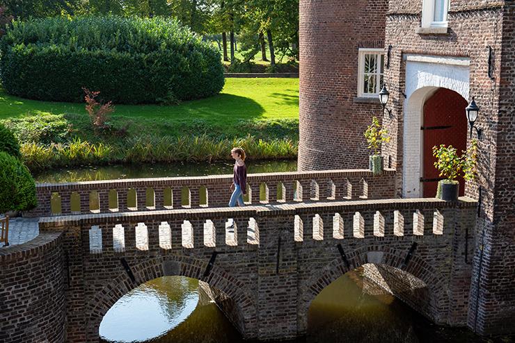 A student walks across the moat using the brick bridge