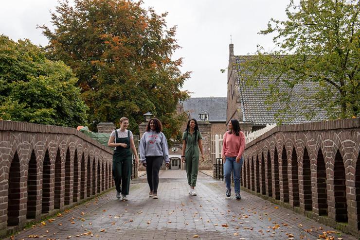 4 students walk across the brick bridge