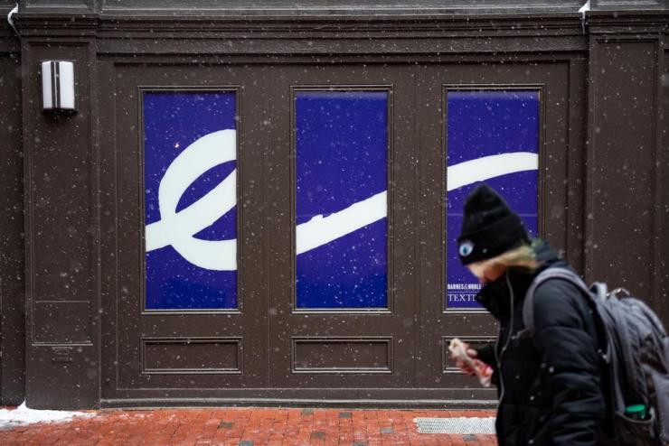 A student walking past a building with the Emerson "E", set in a cursive flourish, on display during a snowy day