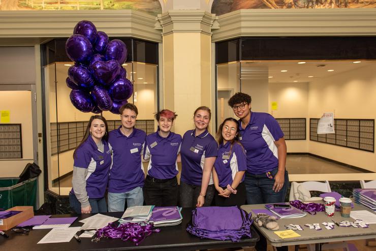 a group of resident assistants wearing purple pose near a table