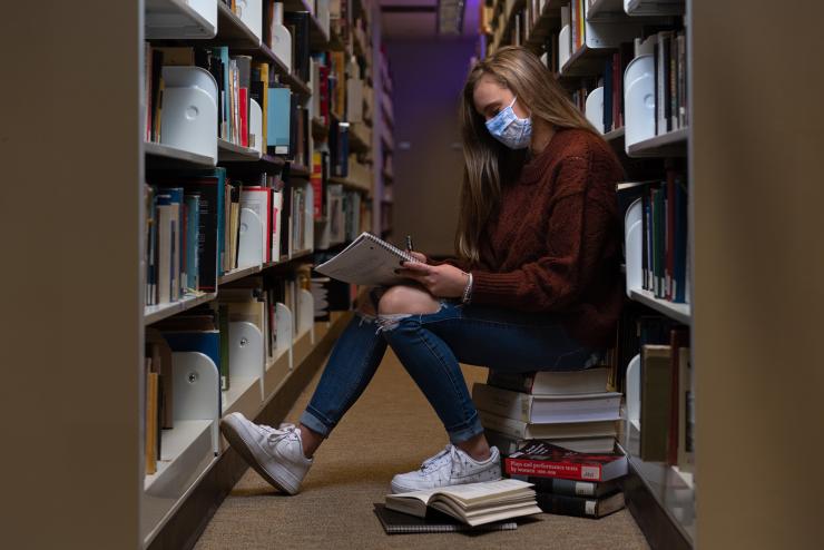 Person sitting in library reading, wearing mask