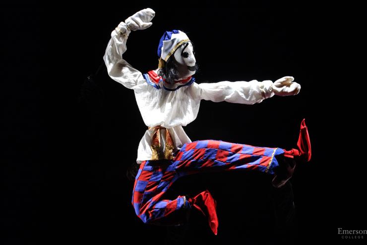 Performer onstage, wearing a costume, jumping in the air and kicking