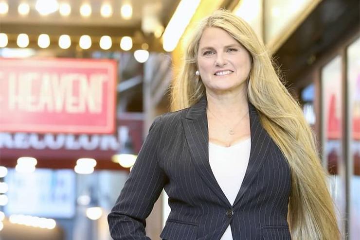 Bonnie Comley smiles while standing in front of a theatre sign