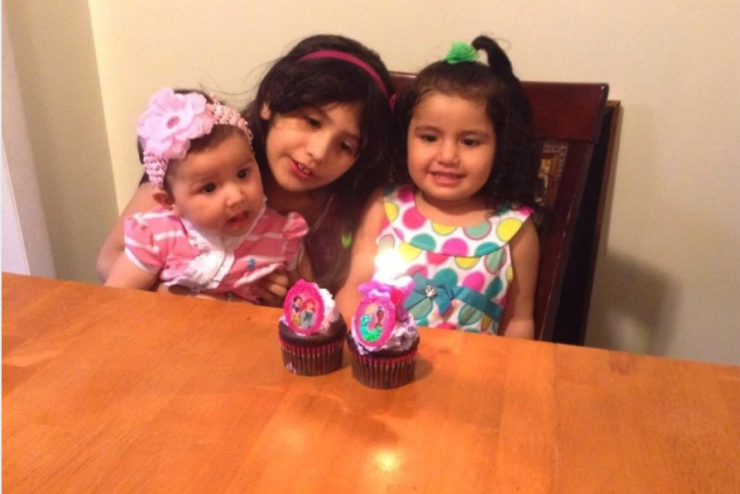Three children sitting on chairs with cupcakes on the table in front of them