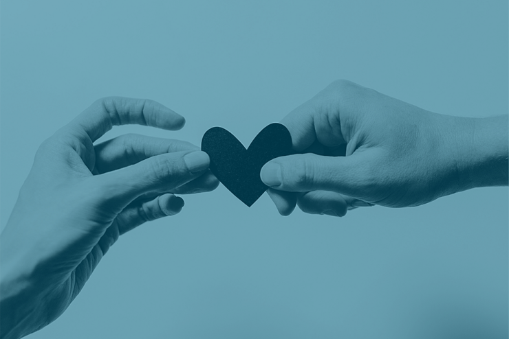 A photo of two hands holding a paper heart with a light blue overlay