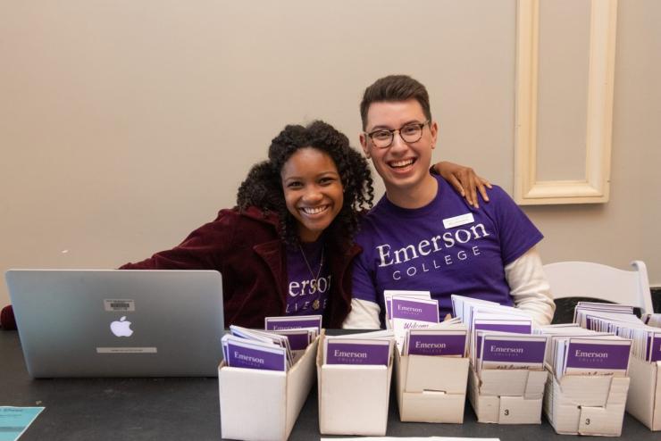 Student volunteers wearing Emerson College t-shirts with Emerson College brochures in front of them