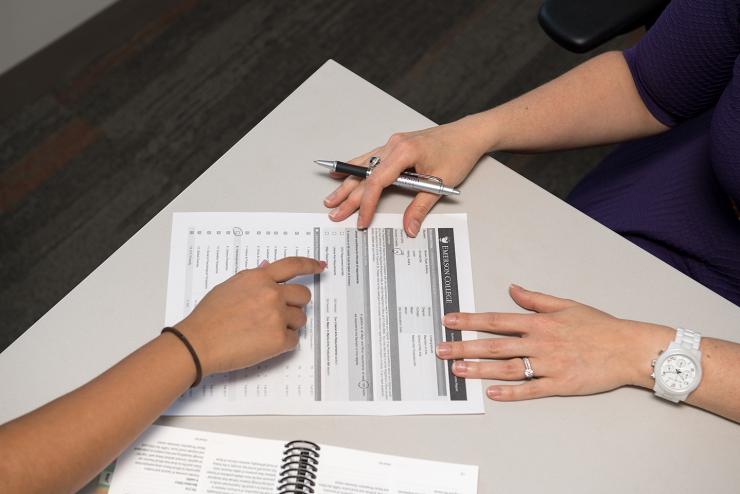 Three students' hands are show on a desk, filling out a form