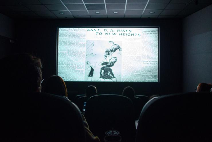 audience members look toward large movie screen in dark room