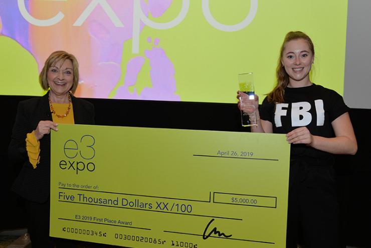 Lu Ann Reeb, Director of Entrepreneurial Studies and Business Studies, and a student hold an oversized check in the amount of $5,000. The student is smiling and also holding a small, clear trophy.