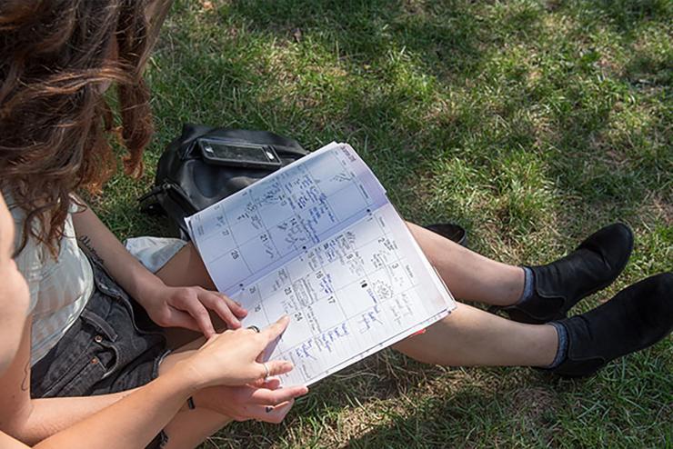 Student sits on grass looking at planning calender