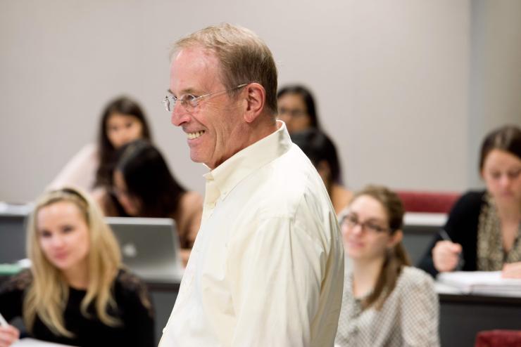An older faculty member smiles in a classroom of students